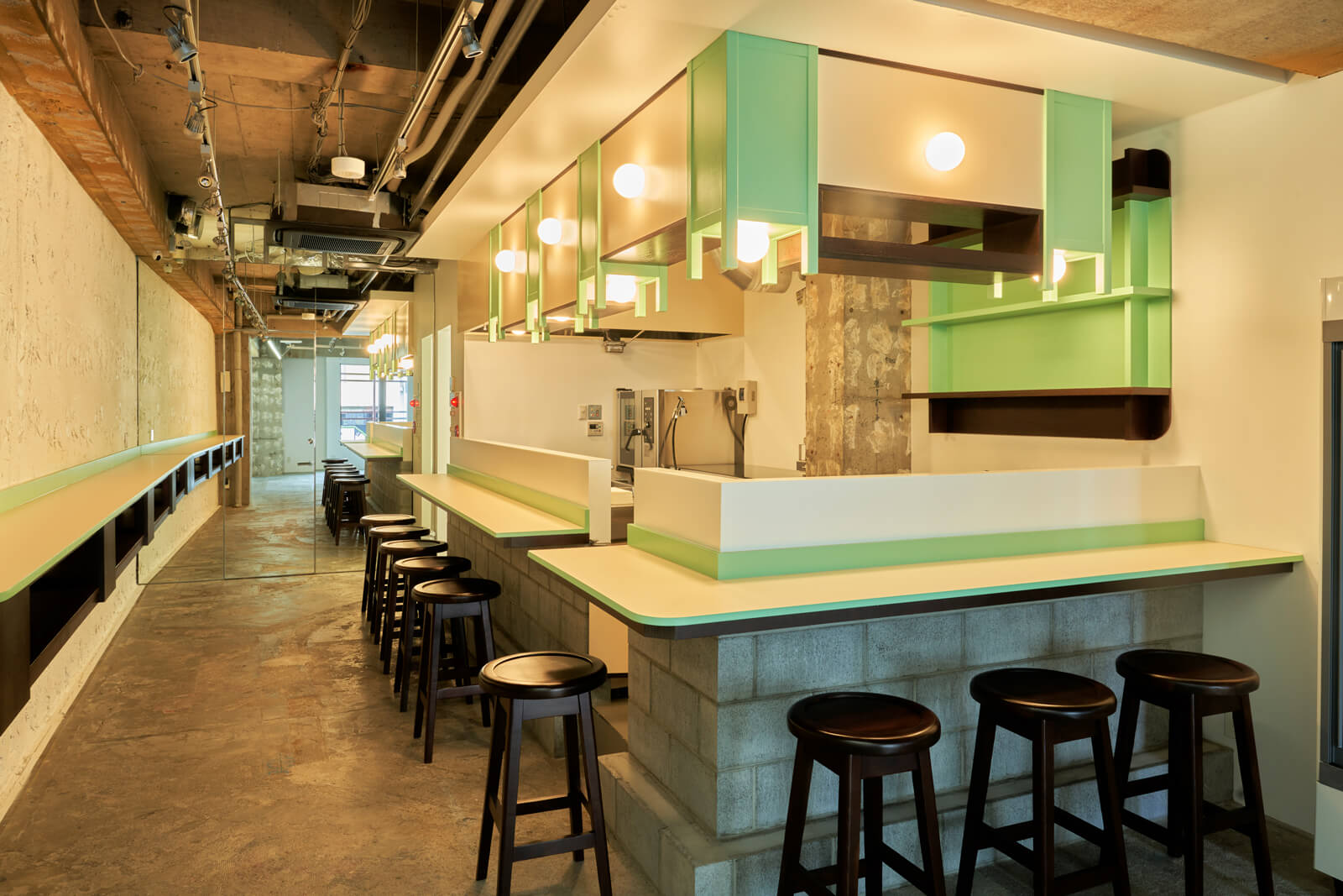 A white counter and concrete walls, with the kitchen visible beyond the counter